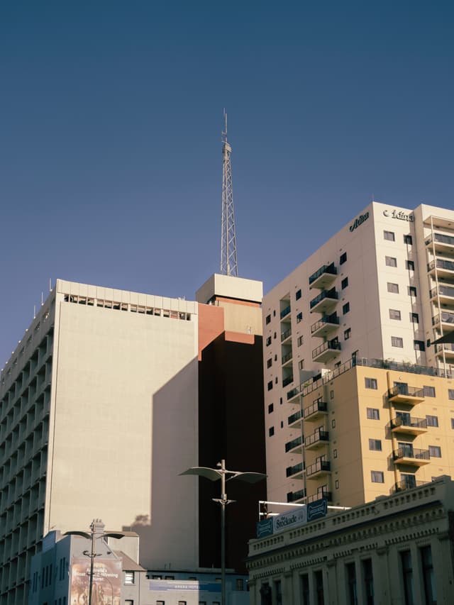 Tall buildings with a central structure featuring a spire, set against a clear blue sky