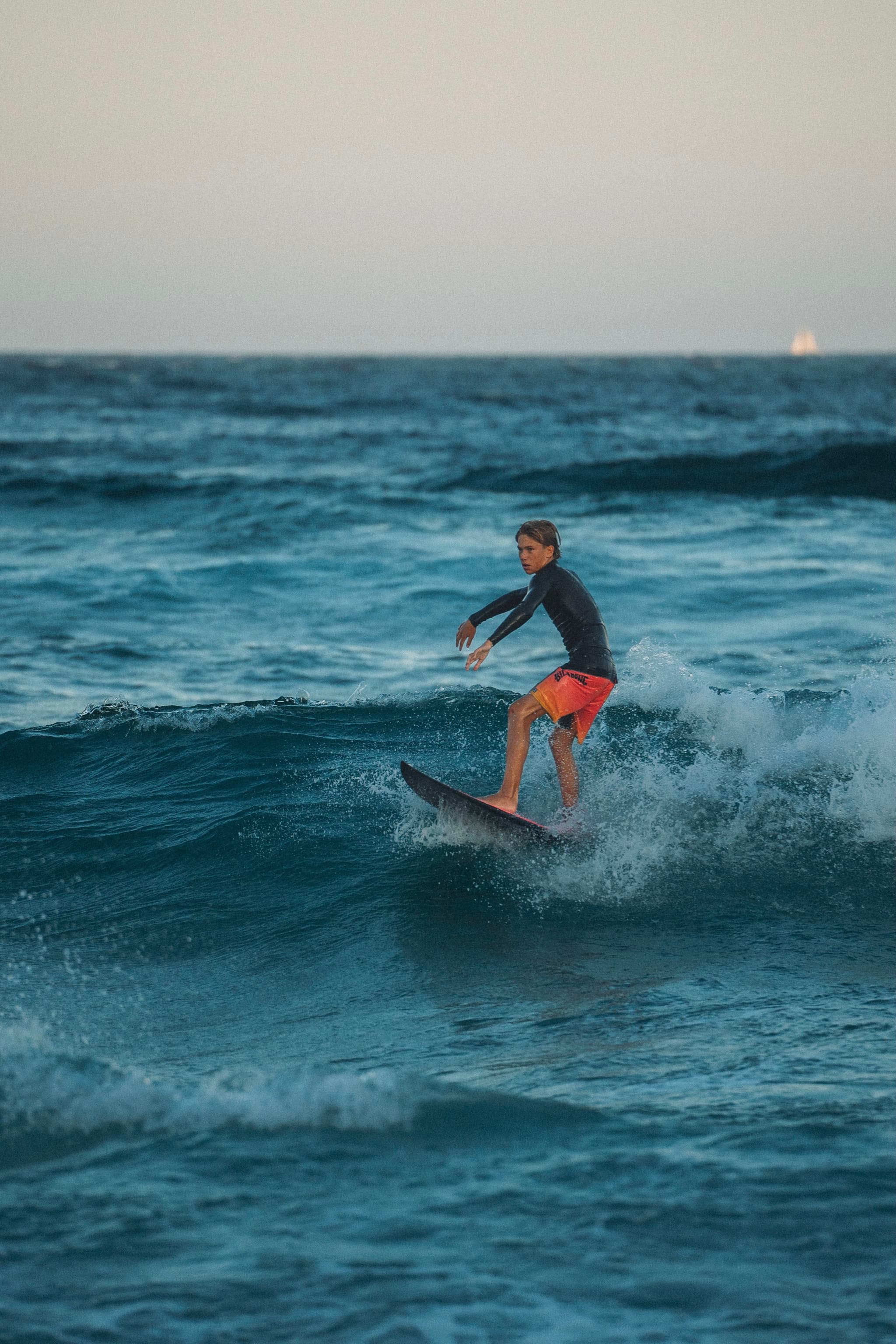 A person surfing on a wave in the ocean, wearing a dark top and red shorts