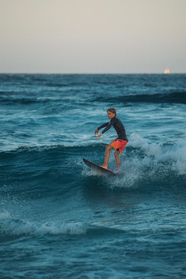 A person surfing on a wave in the ocean, wearing a dark top and red shorts