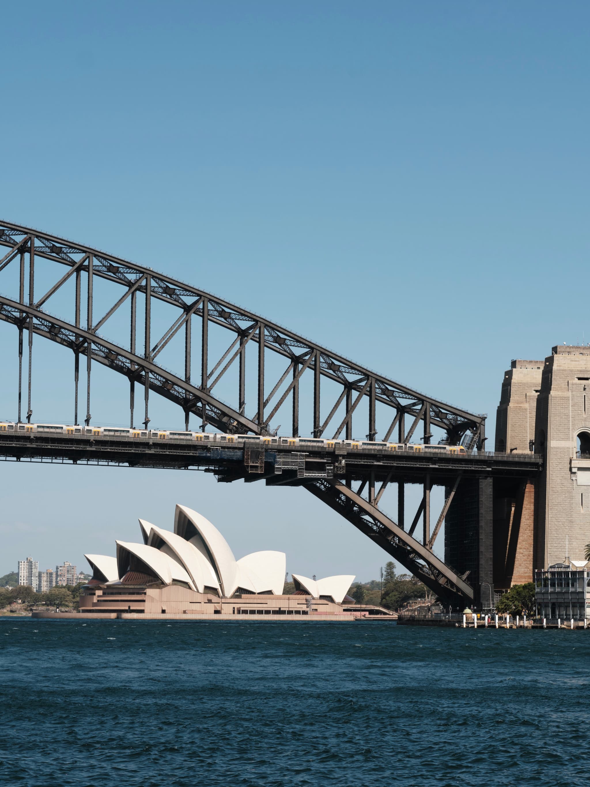 Sydney Harbour Bridge with the Sydney Opera House in the background, set against a clear blue sky