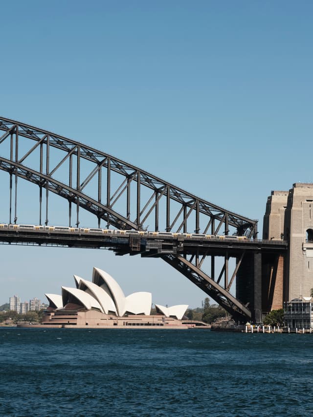 Sydney Harbour Bridge with the Sydney Opera House in the background, set against a clear blue sky