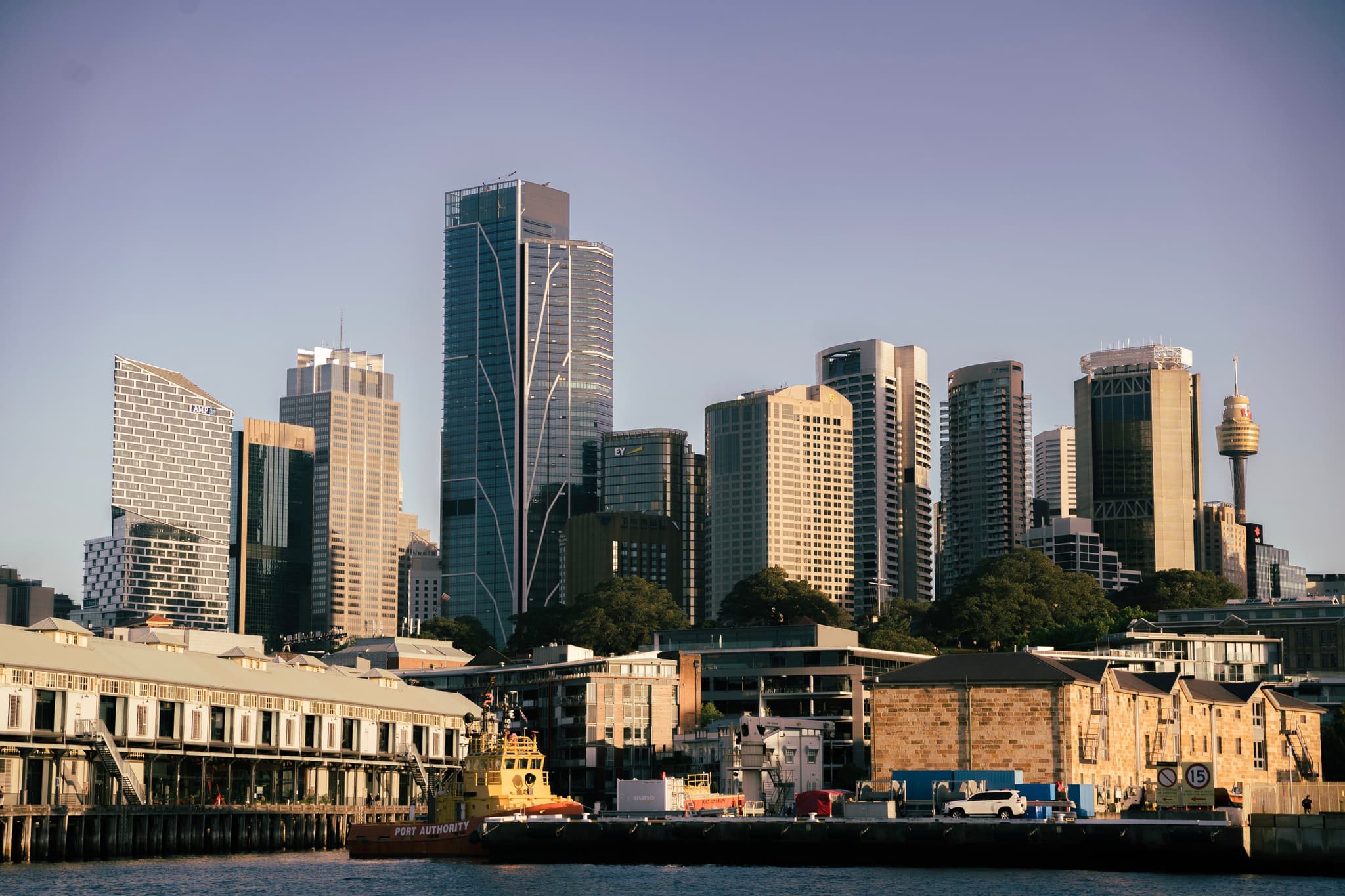 A city skyline with modern skyscrapers and a waterfront area in the foreground, under a clear sky