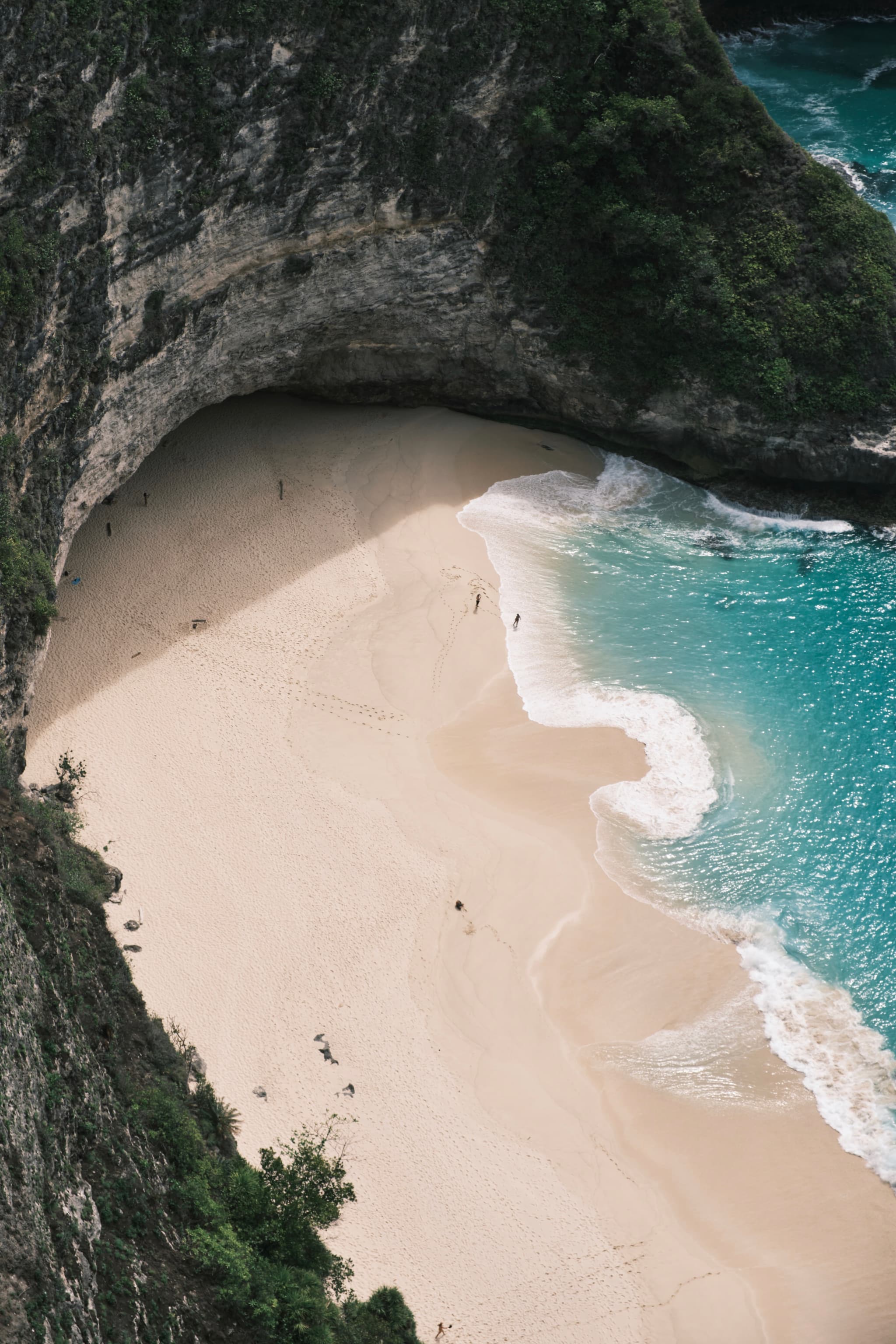 A secluded beach with white sand and turquoise water, surrounded by steep cliffs and lush greenery