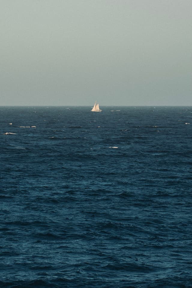 A sailboat on the horizon of a vast, calm ocean under a clear sky