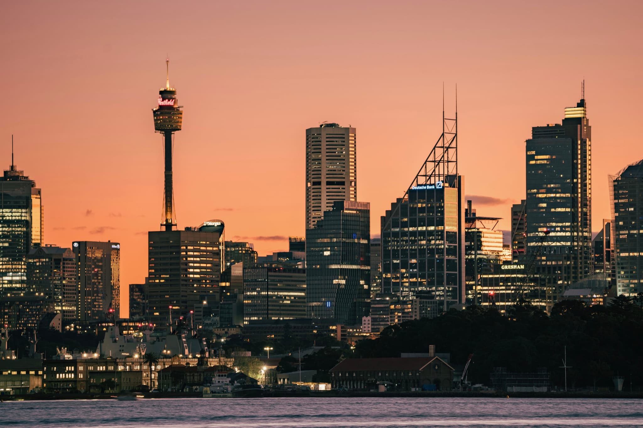 A city skyline at sunset with tall buildings silhouetted against an orange sky
