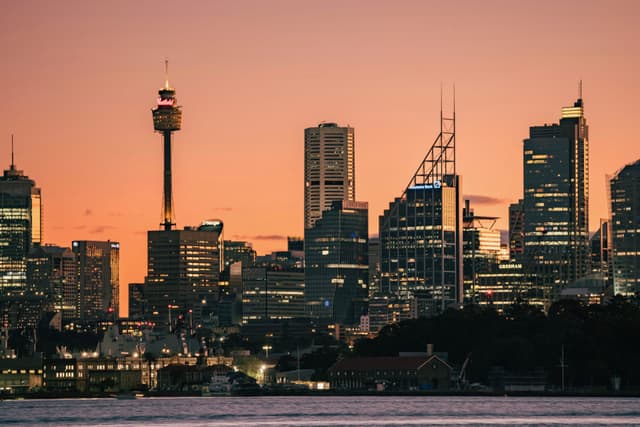 A city skyline at sunset with tall buildings silhouetted against an orange sky