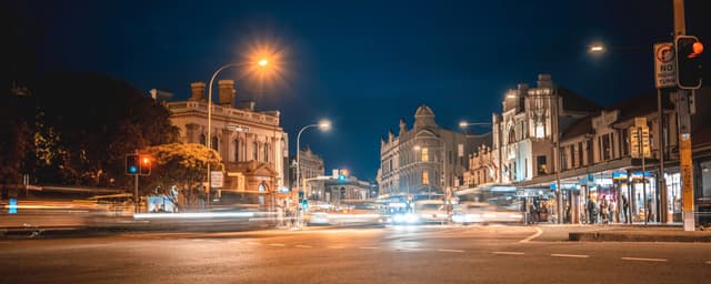 A bustling city street at night with blurred lights from moving vehicles, historic buildings, and illuminated streetlights