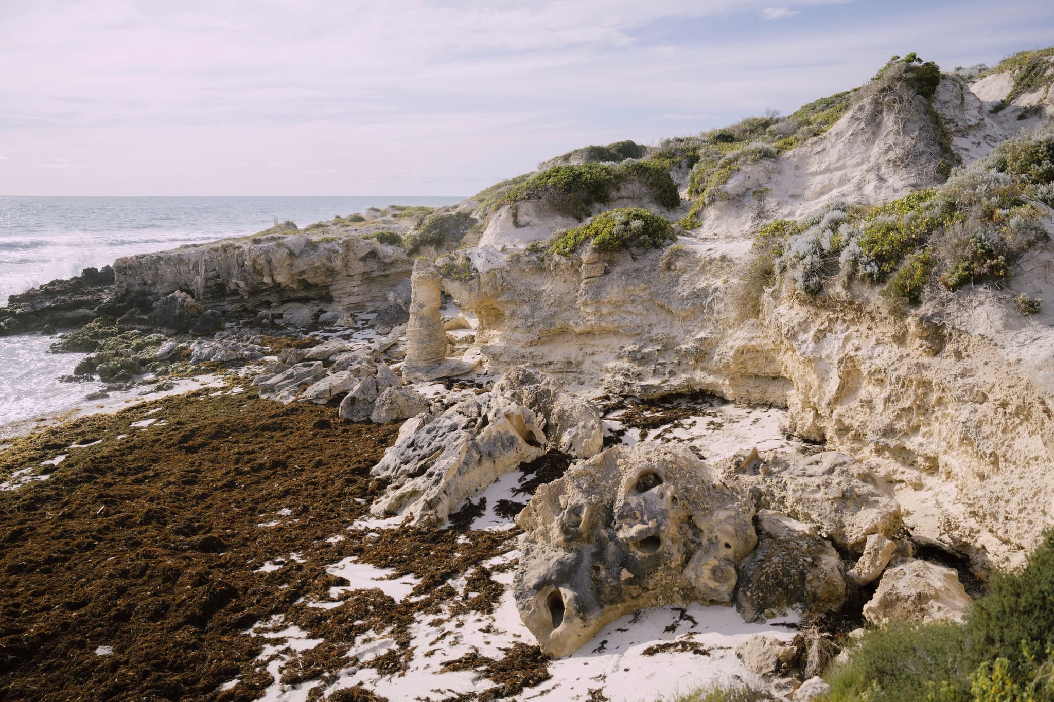 A rocky coastal landscape with eroded cliffs, sparse vegetation, and a view of the ocean