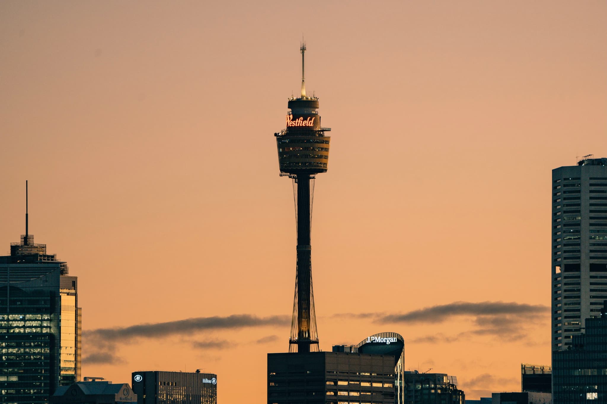 A city skyline at sunset featuring a prominent tower with an observation deck, surrounded by other buildings