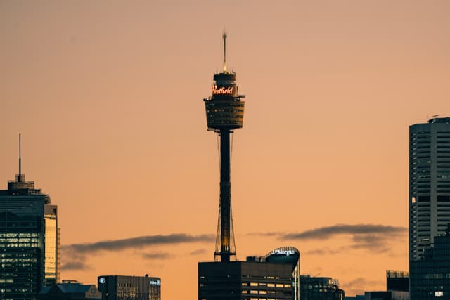 A city skyline at sunset featuring a prominent tower with an observation deck, surrounded by other buildings