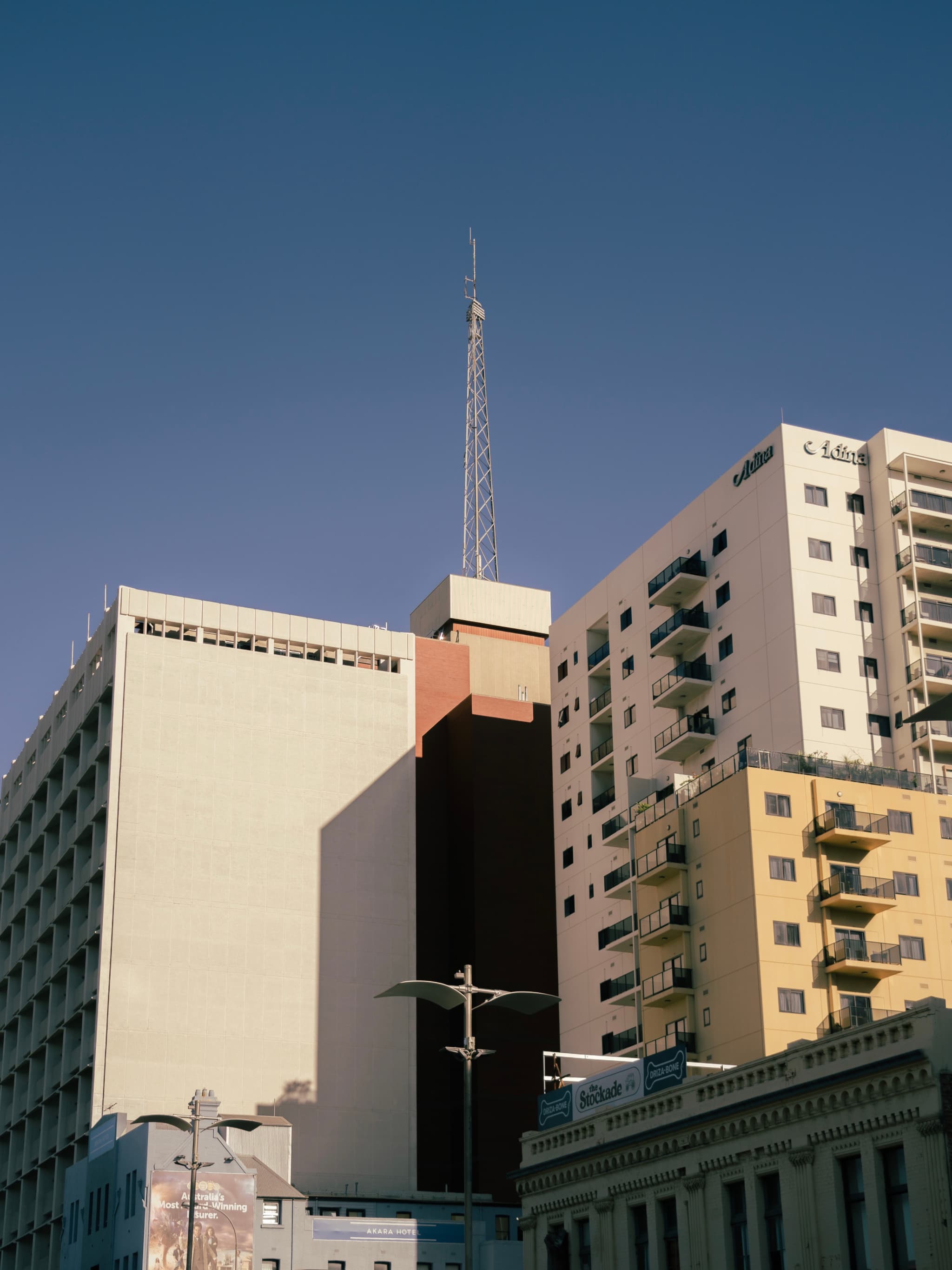 Tall buildings with a central structure featuring a spire, set against a clear blue sky
