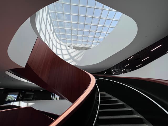 A modern, curved staircase with wooden railings and a glass ceiling allowing natural light to illuminate the space