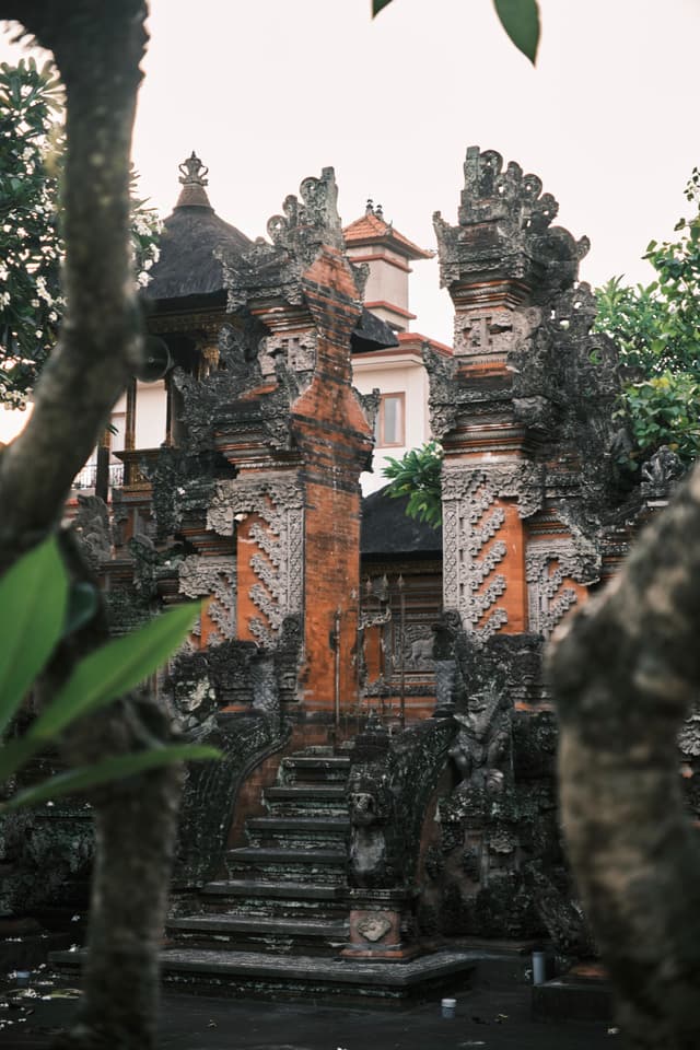 An ornate, traditional Balinese gate with intricate carvings and stone steps, surrounded by lush greenery