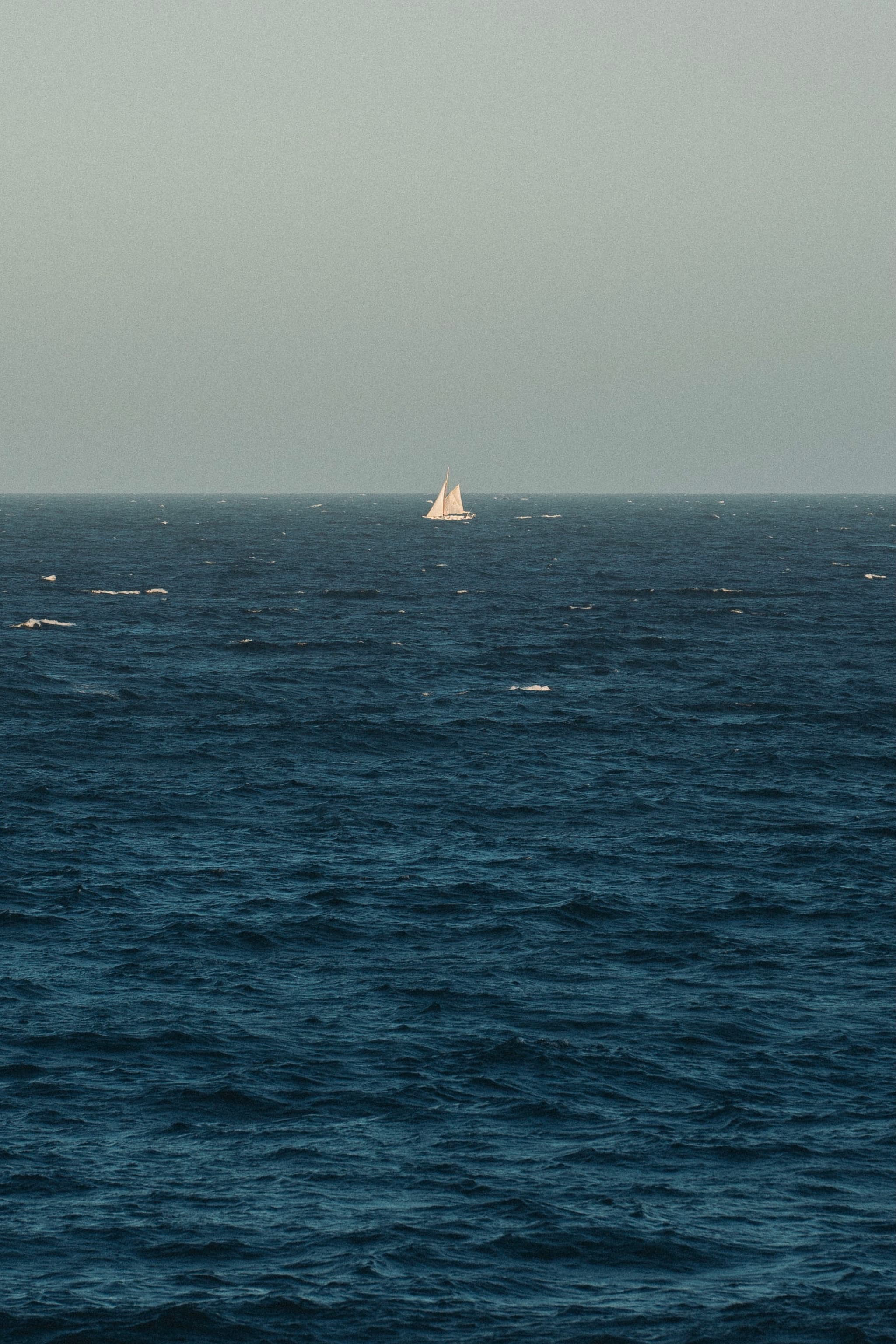 A sailboat on the horizon of a vast, calm ocean under a clear sky