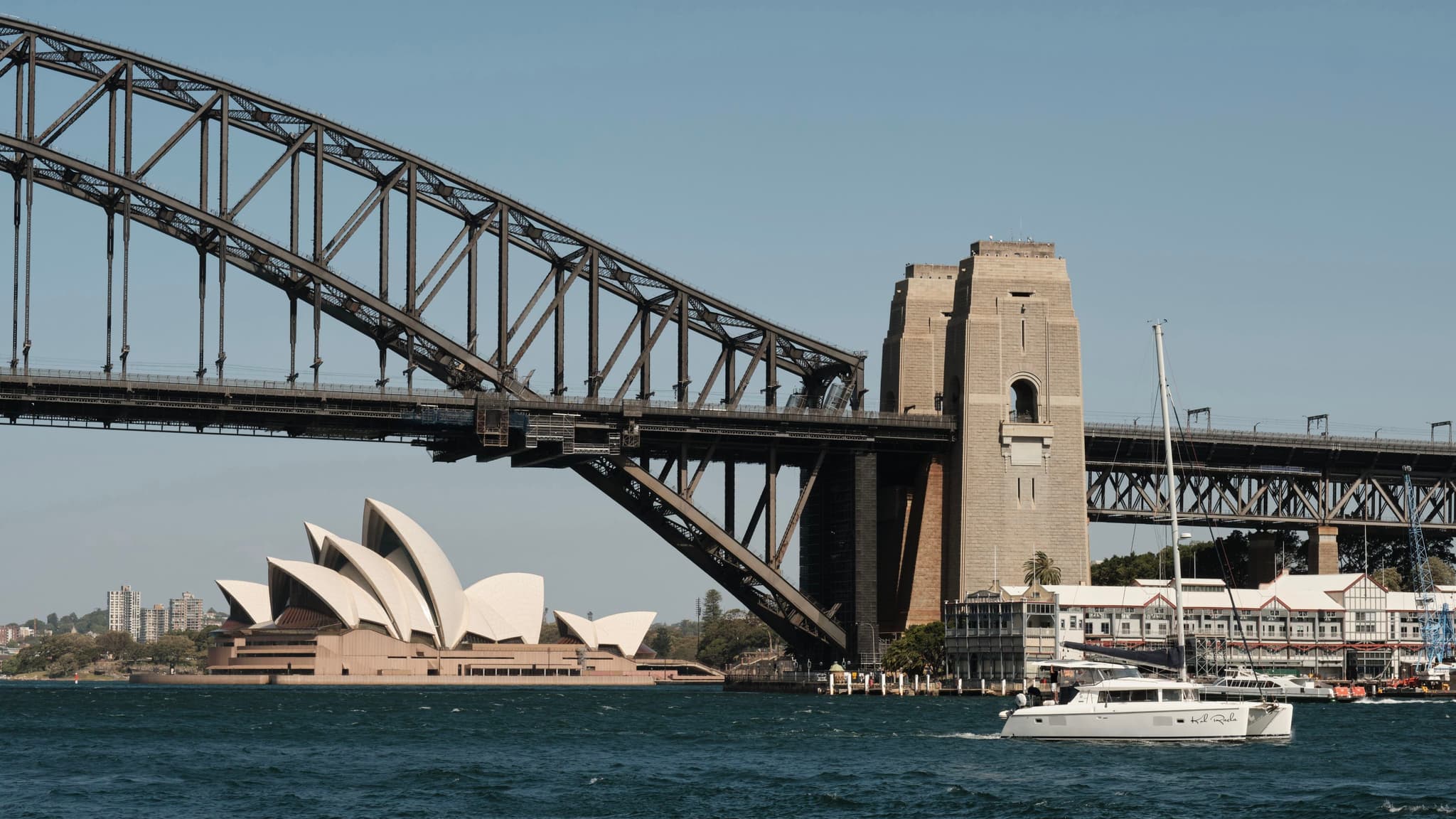 A view of the Sydney Harbour Bridge with the Sydney Opera House in the background and a boat on the water