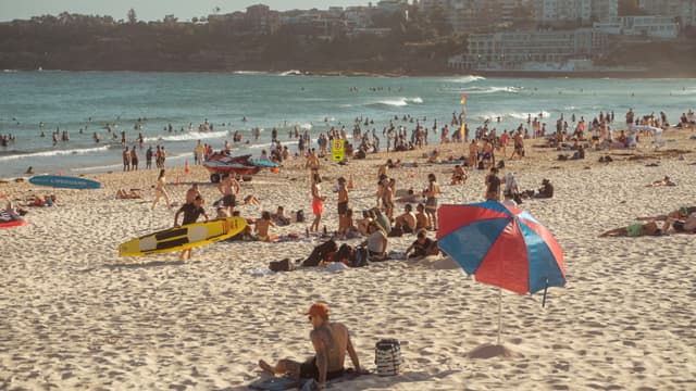 A crowded beach with people sunbathing, swimming, and relaxing under umbrellas
