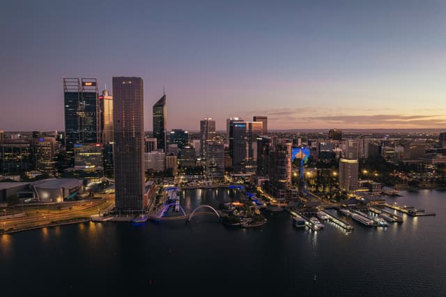 A city skyline at dusk with illuminated skyscrapers and a waterfront, reflecting lights on the water