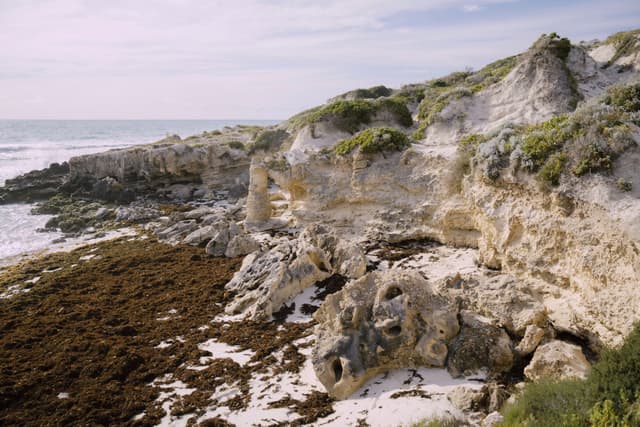 A rocky coastal landscape with eroded cliffs, sparse vegetation, and a view of the ocean