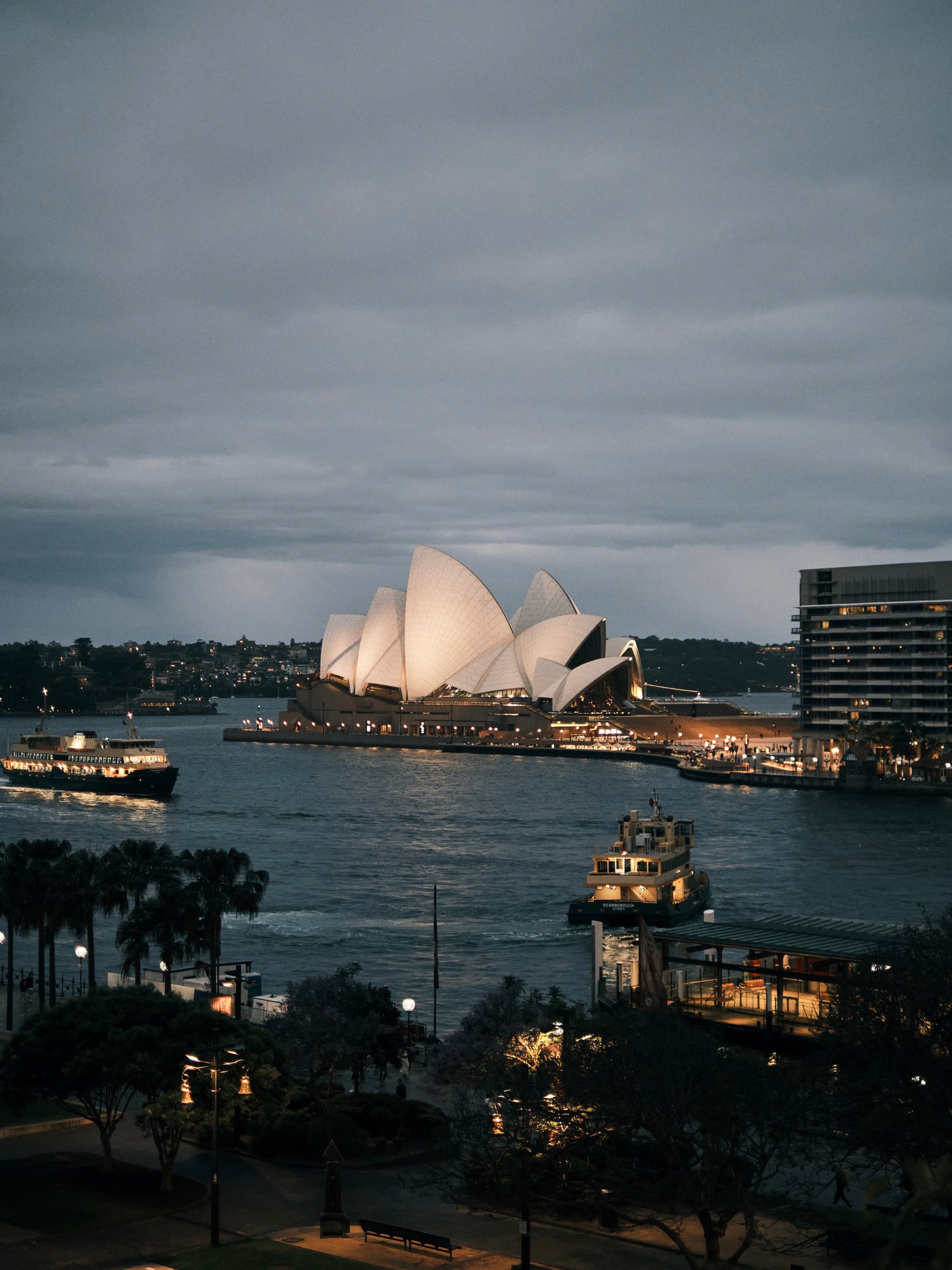 The Sydney Opera House illuminated at dusk, with boats on the water and a cloudy sky overhead
