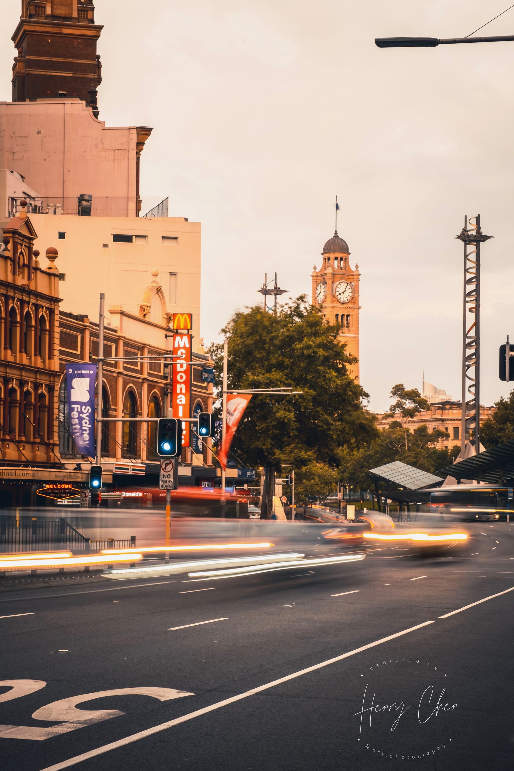 A city street scene with blurred motion from passing vehicles, featuring historic buildings and a clock tower in the background